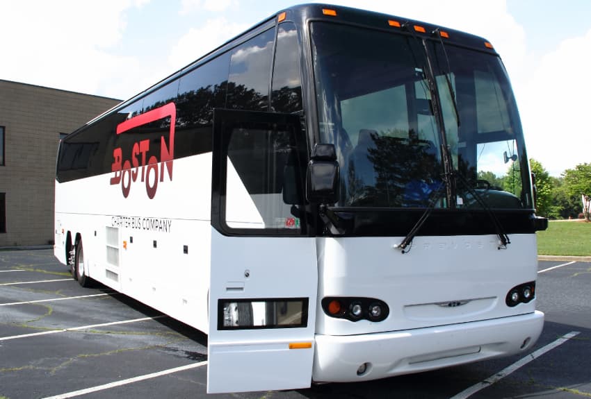 A branded Boston Charter Bus Company charter bus parks in an empty parking lot, door open wide for passengers to board