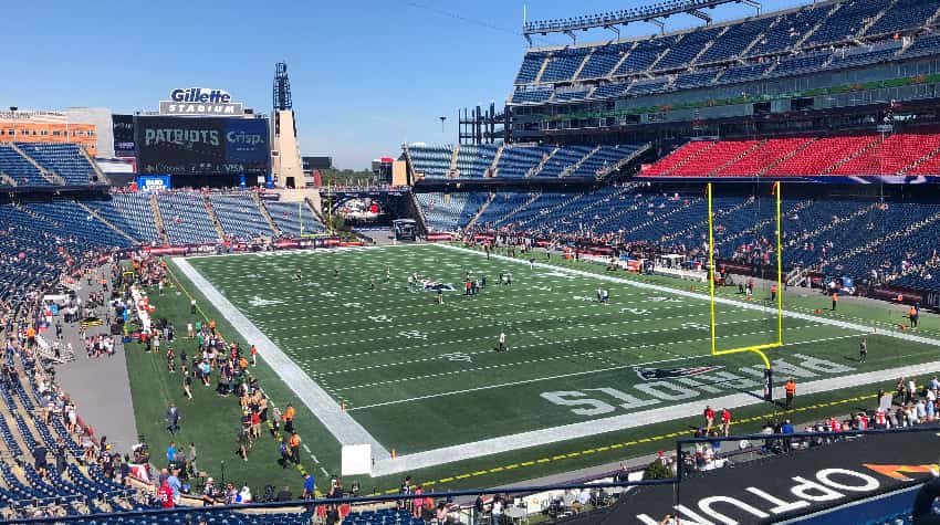Gillette Stadium on a sunny day, fans and players walking around on the field